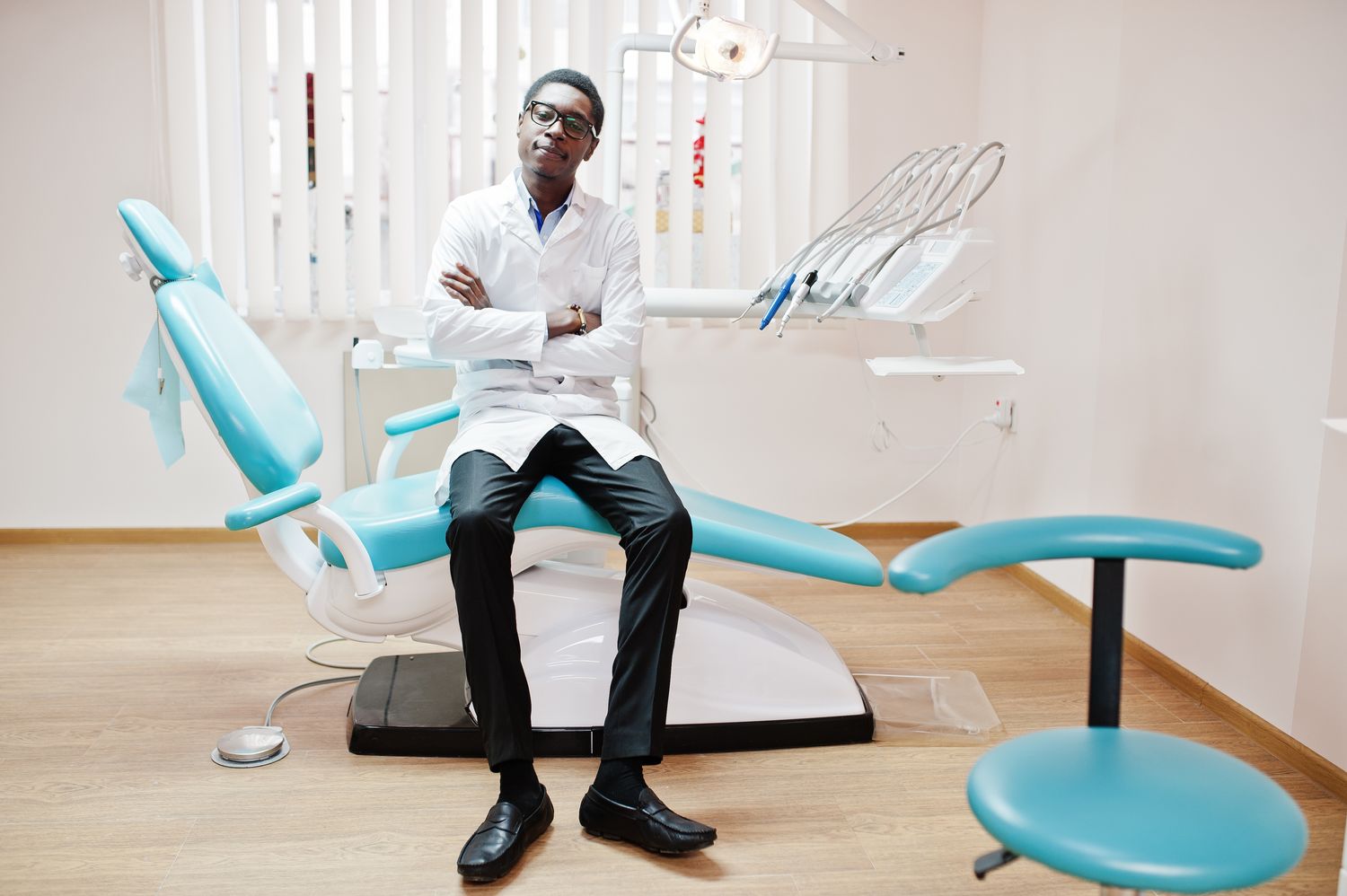 African american male doctor in glasses sitting at dentist chair in dental clinic.