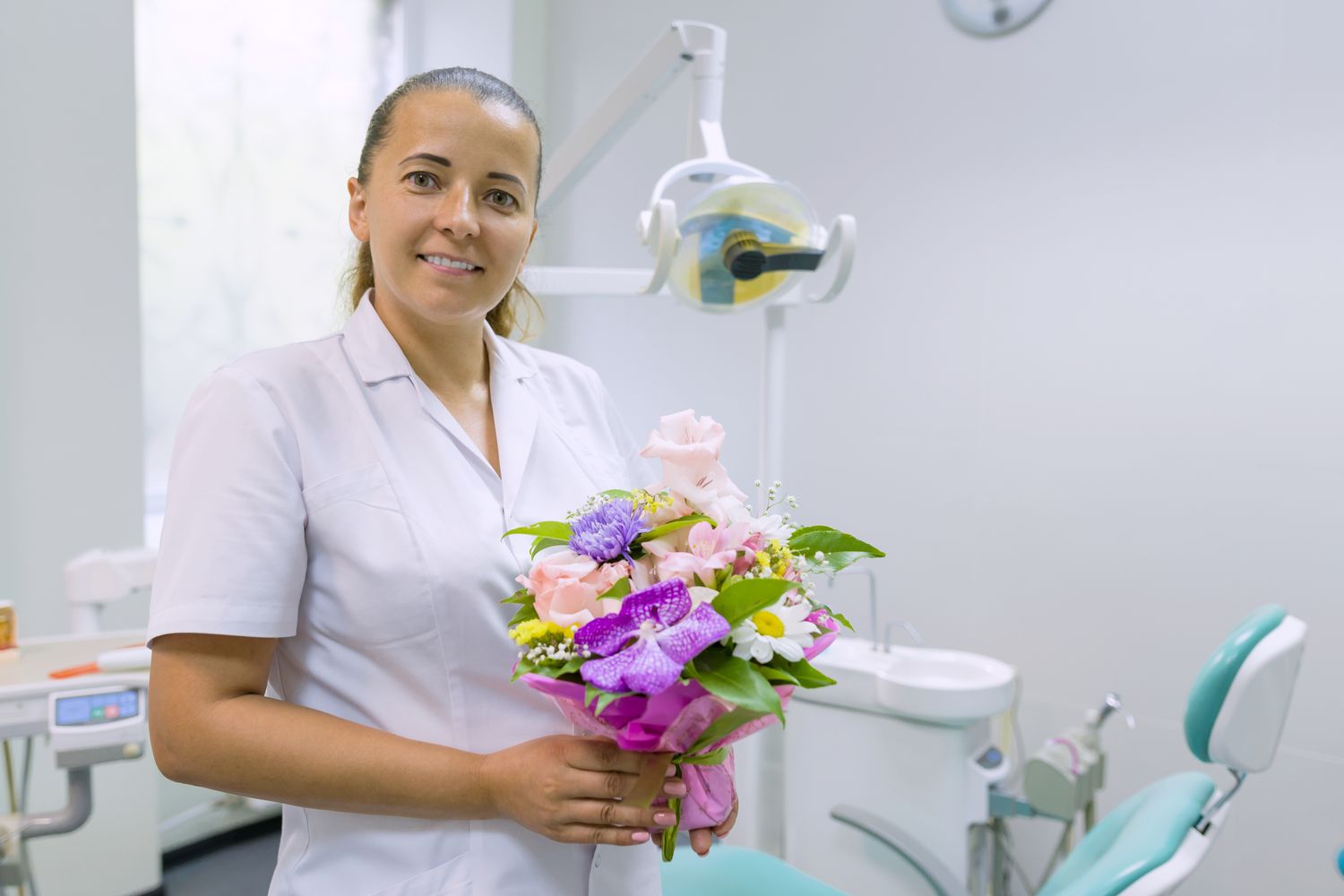 Female dentist smiling, with a bouquet of flowers, in dental office. National dentist's day