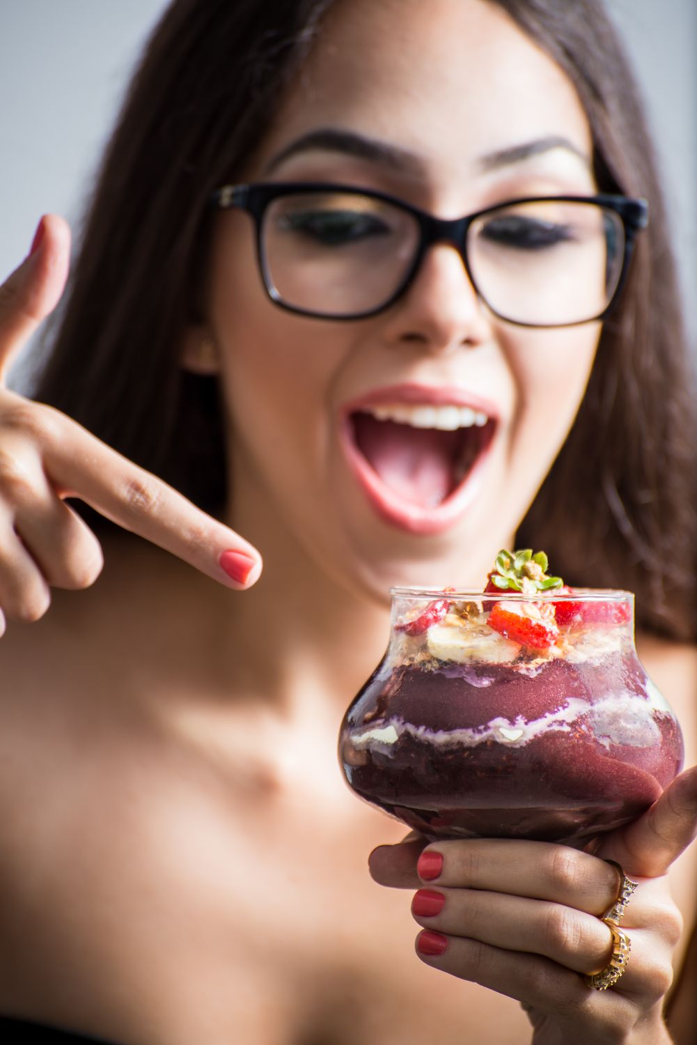 Female with glasses holding bowl acai with strawberries and banana